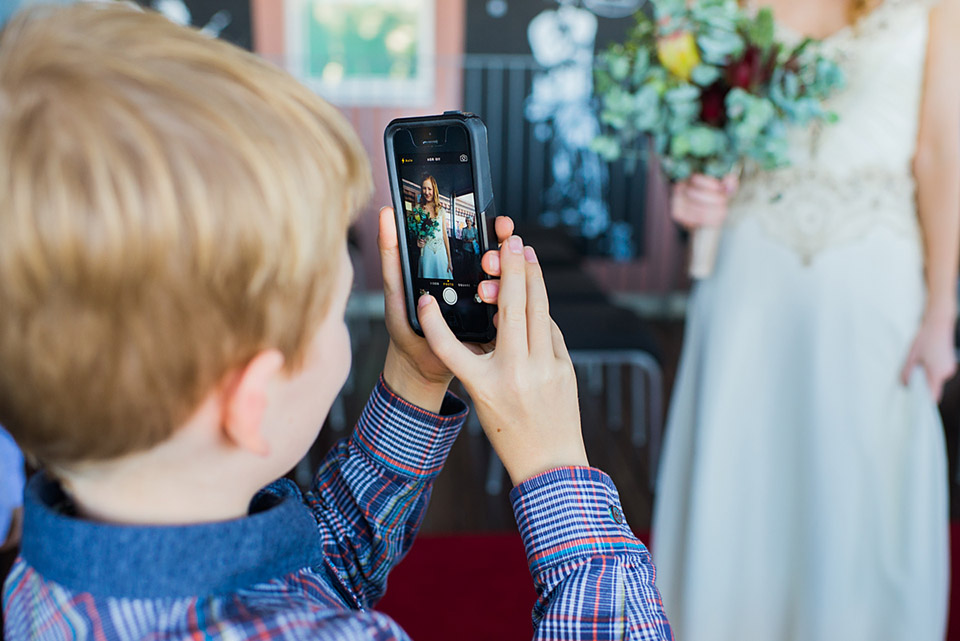 A child taking a photo of the bride at the ceremony
