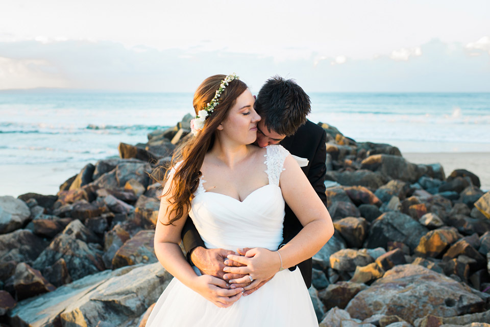 Portrait of Tenielle and Mick hugging each other at Noosa Main Beach on their wedding day.