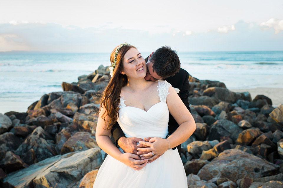 Portrait of Tenielle and Mick hugging each other at Noosa Main Beach on their wedding day.