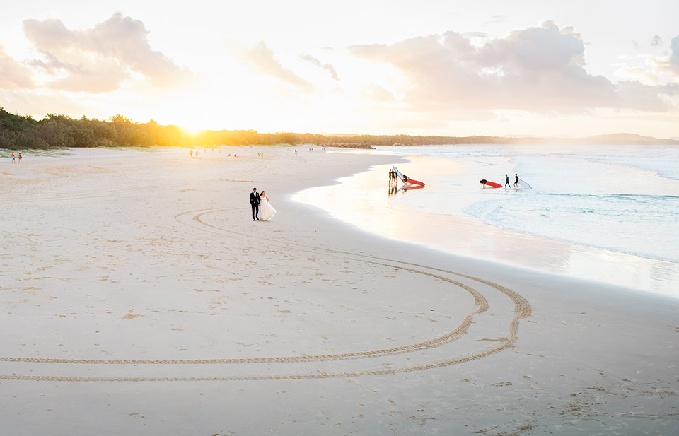 Photo of bride and groom walking along Noosa beach on their wedding day