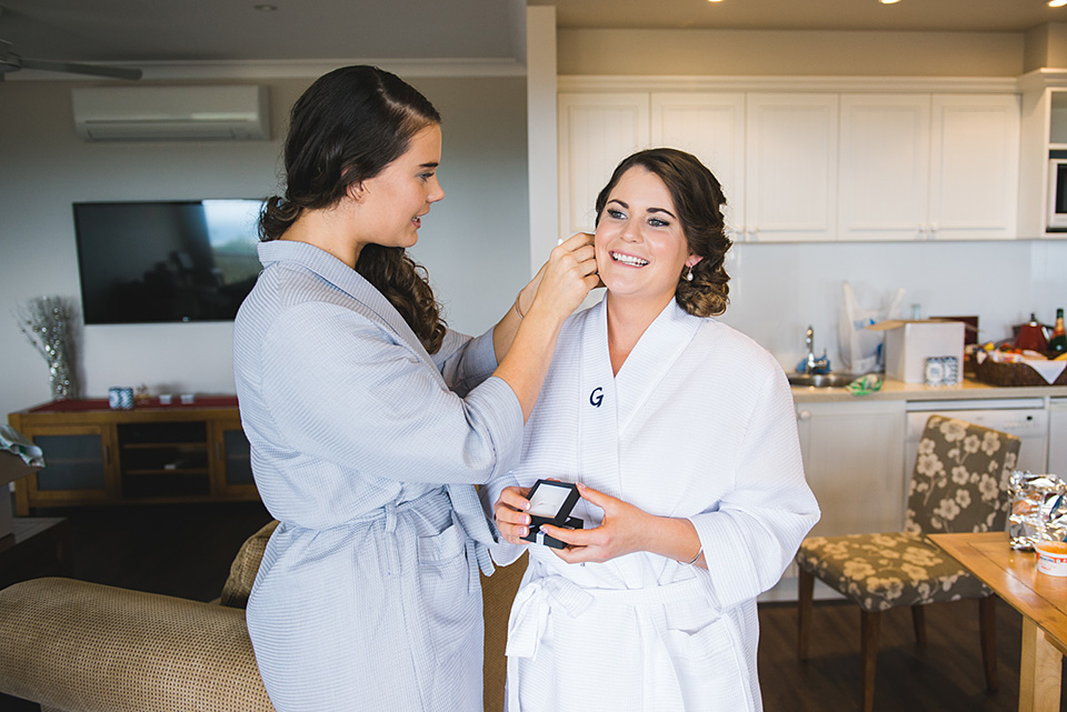Bridesmaid putting earrings on the Bride.