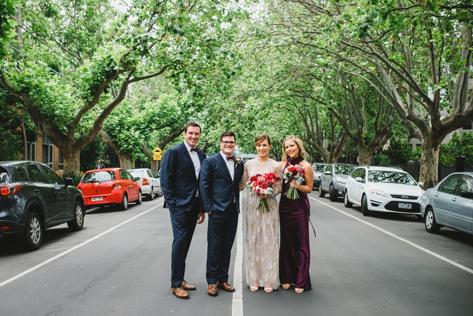 Photo of the bridal party in the middle of the road, underneath trees.