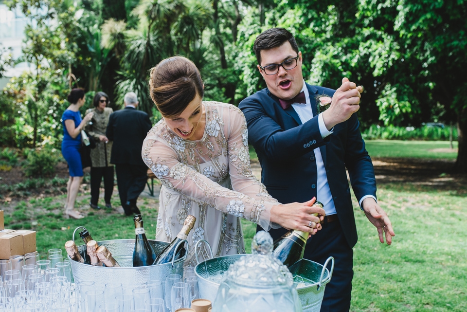 The bride and groom popping a massive bottle of champagne in celebration.