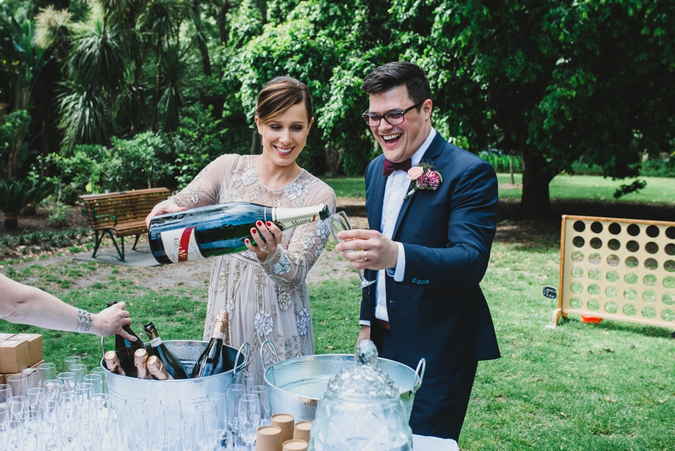 The bride and groom pouring a glass of champagne from a massive bottle in celebration.